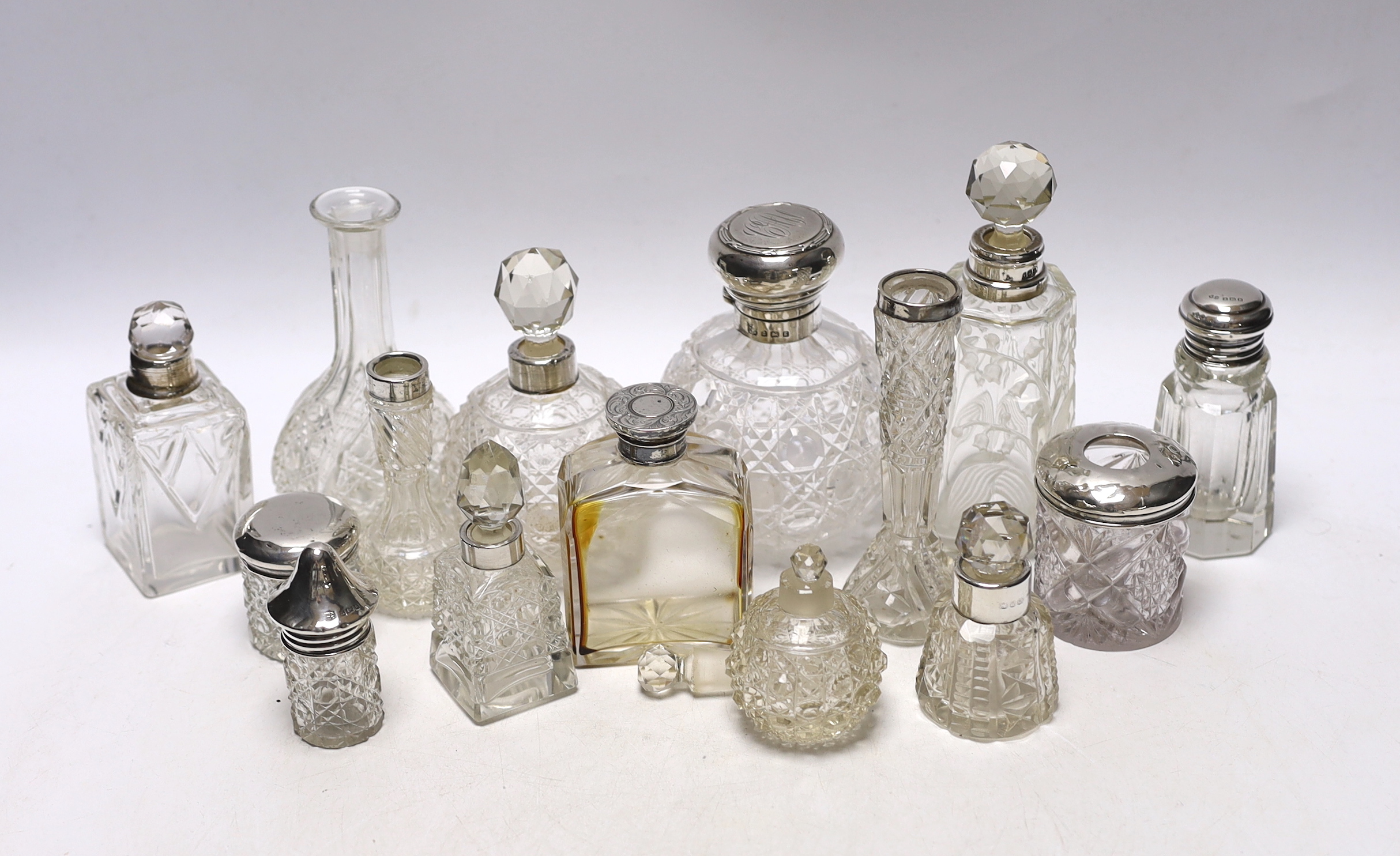 Fourteen assorted silver topped scent or toilet bottles and one without a mount, largest 14.7cm.